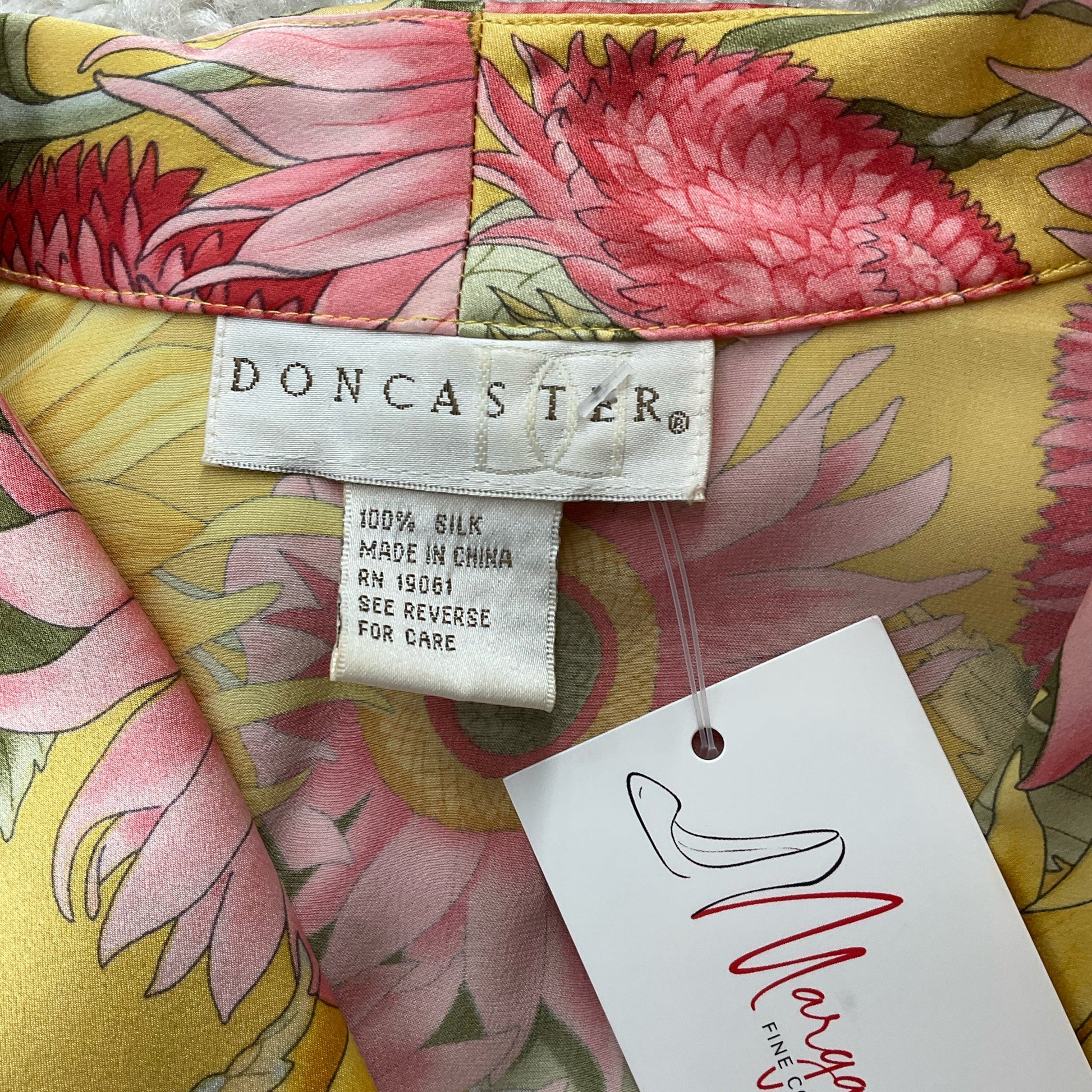 Close-up of Doncaster brand label on yellow/pink floral silk top, size small, highlighting 100% silk material and consignment fashion appeal.