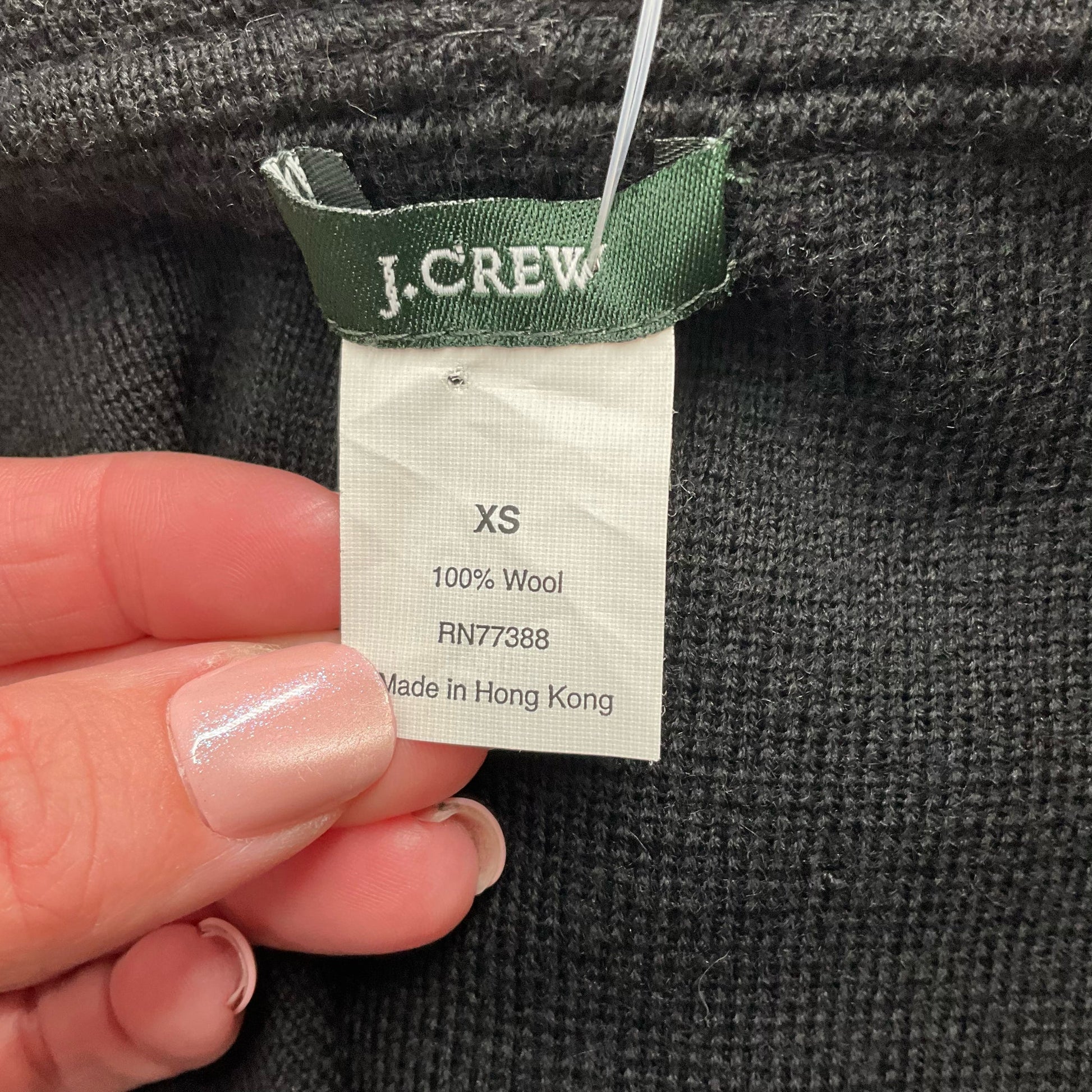 Fabric tag of J Crew Black Solid Pre-Owned Top - Size XS showing 100% wool material and made in Hong Kong.