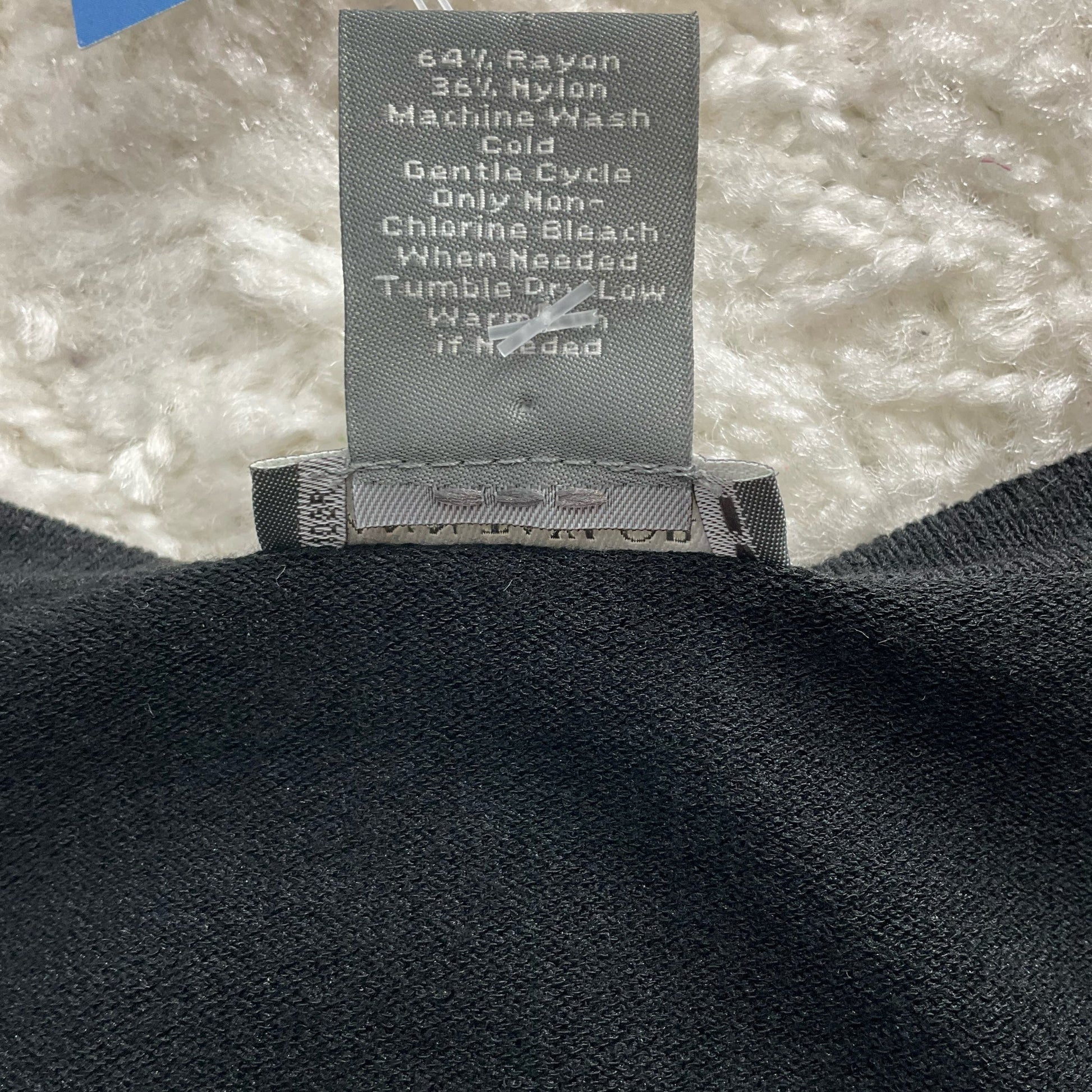 Fabric care label of Ann Taylor black shrug, showing rayon-nylon blend and washing instructions for proper garment maintenance.