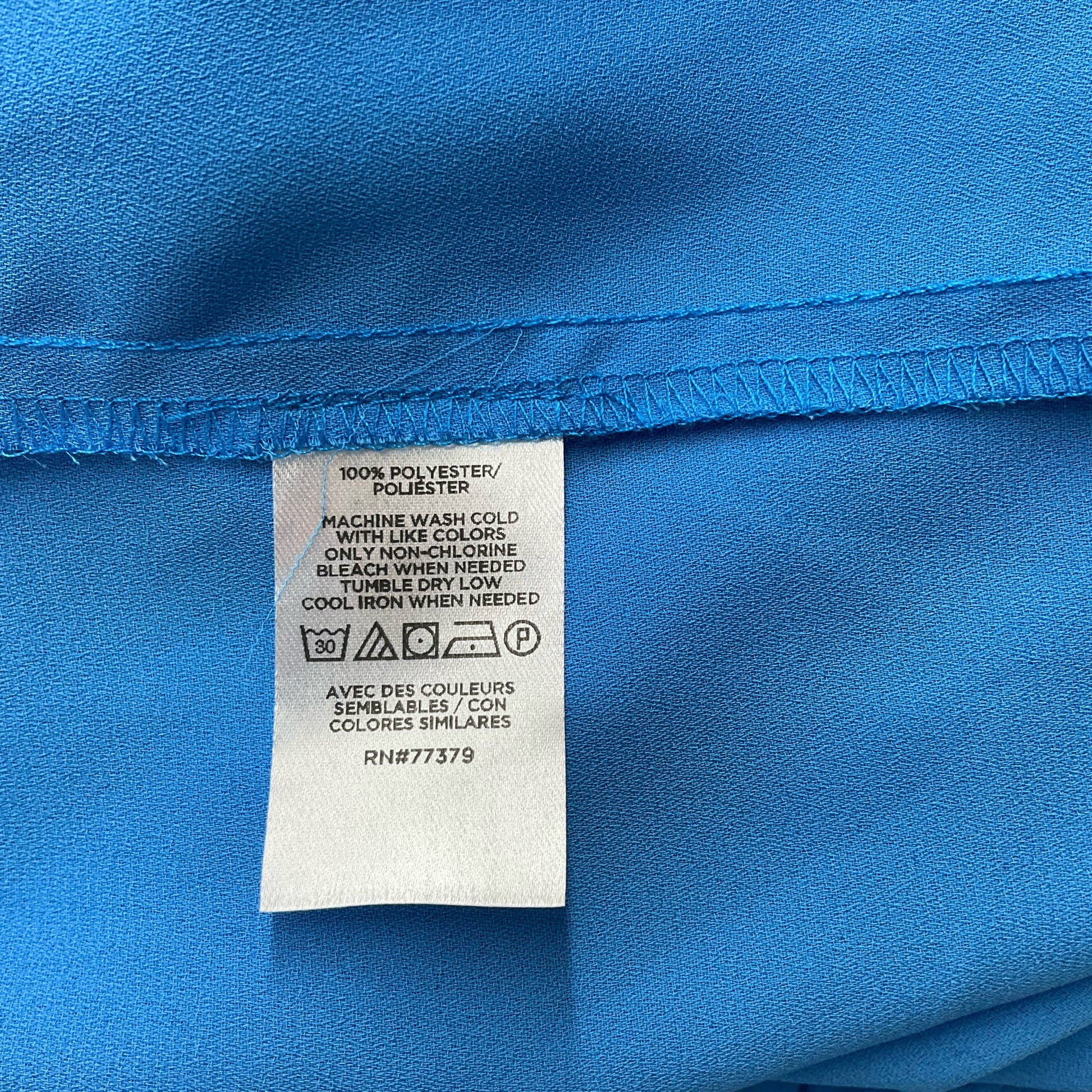 Fabric care label of Ann Taylor Blue Solid Pre-Owned Top - Size Large, made of 100% polyester with machine wash instructions.