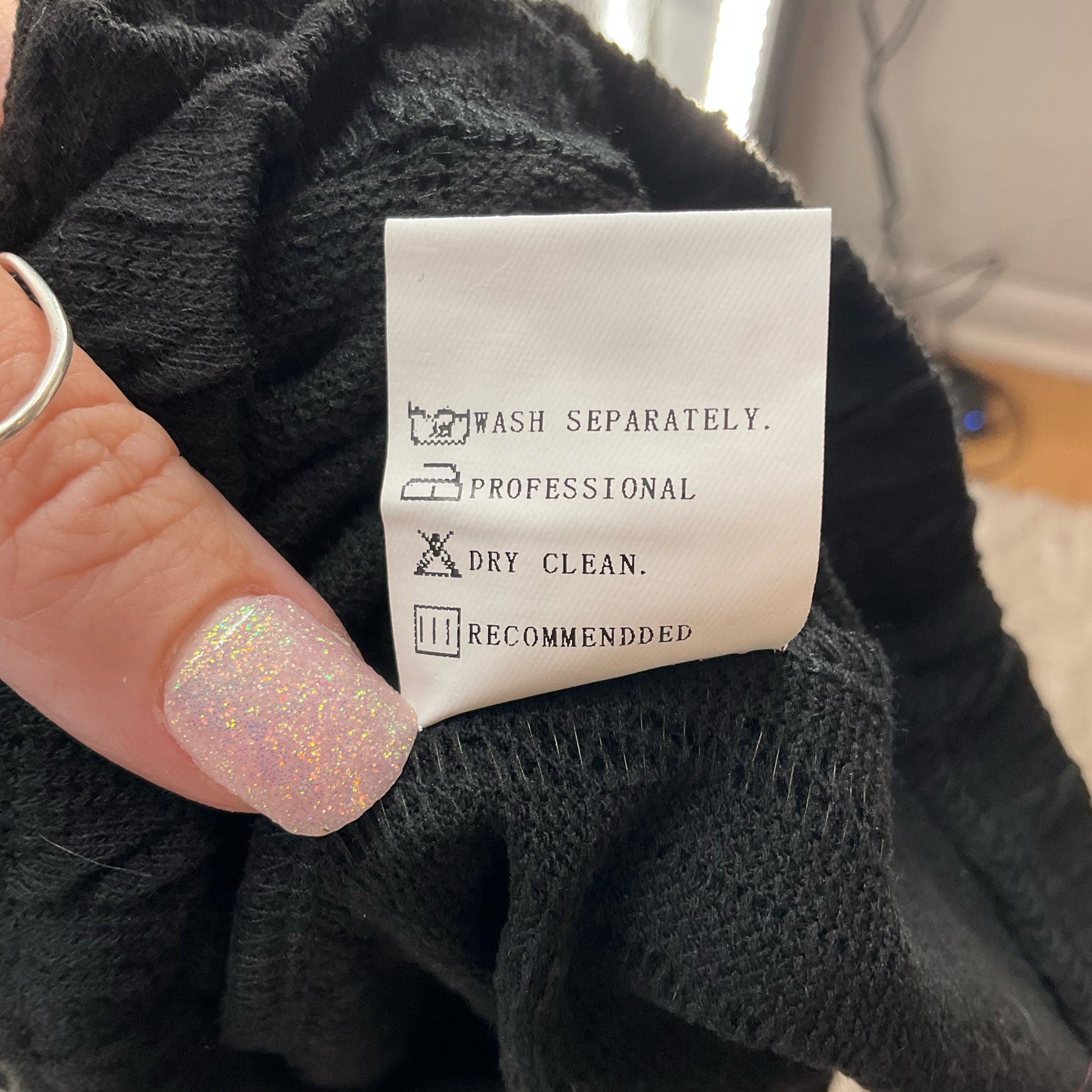Care label on Noracora black sweater size XL, recommending professional dry clean and separate washing for fabric maintenance.
