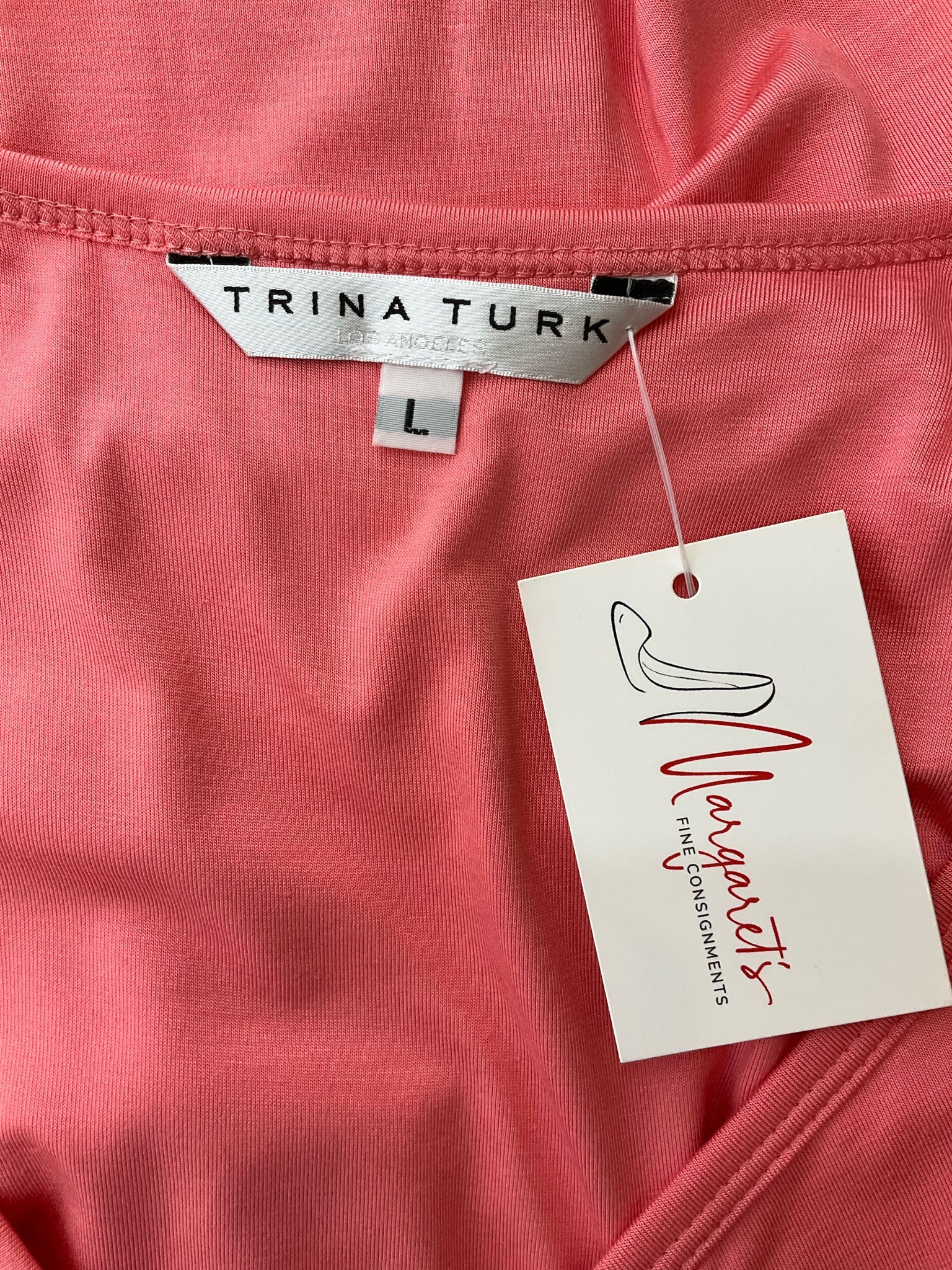Close-up of Trina Turk label and size tag on coral dress, confirming size L. Designer resort wear from Margaret's Fine Consignments.