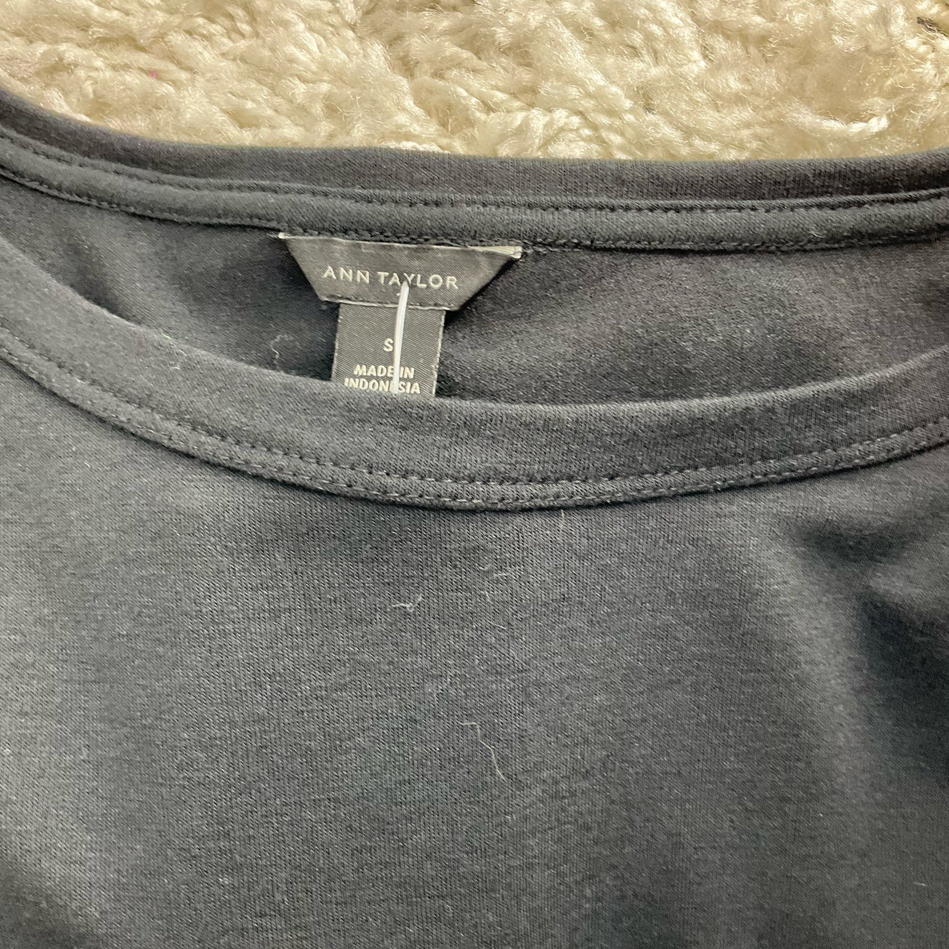 Close-up of Ann Taylor brand label on Black Solid Pre-Owned Top - Size Small, confirming size and origin as Made in Indonesia.