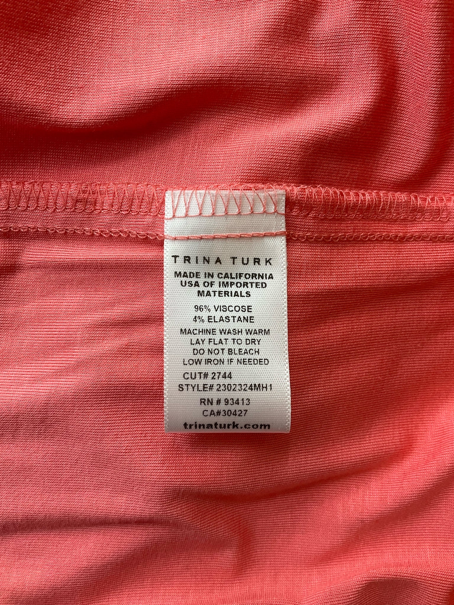 Fabric care label of Trina Turk coral midi dress, made in California with viscose and elastane. Machine washable, style 2302324MH1.