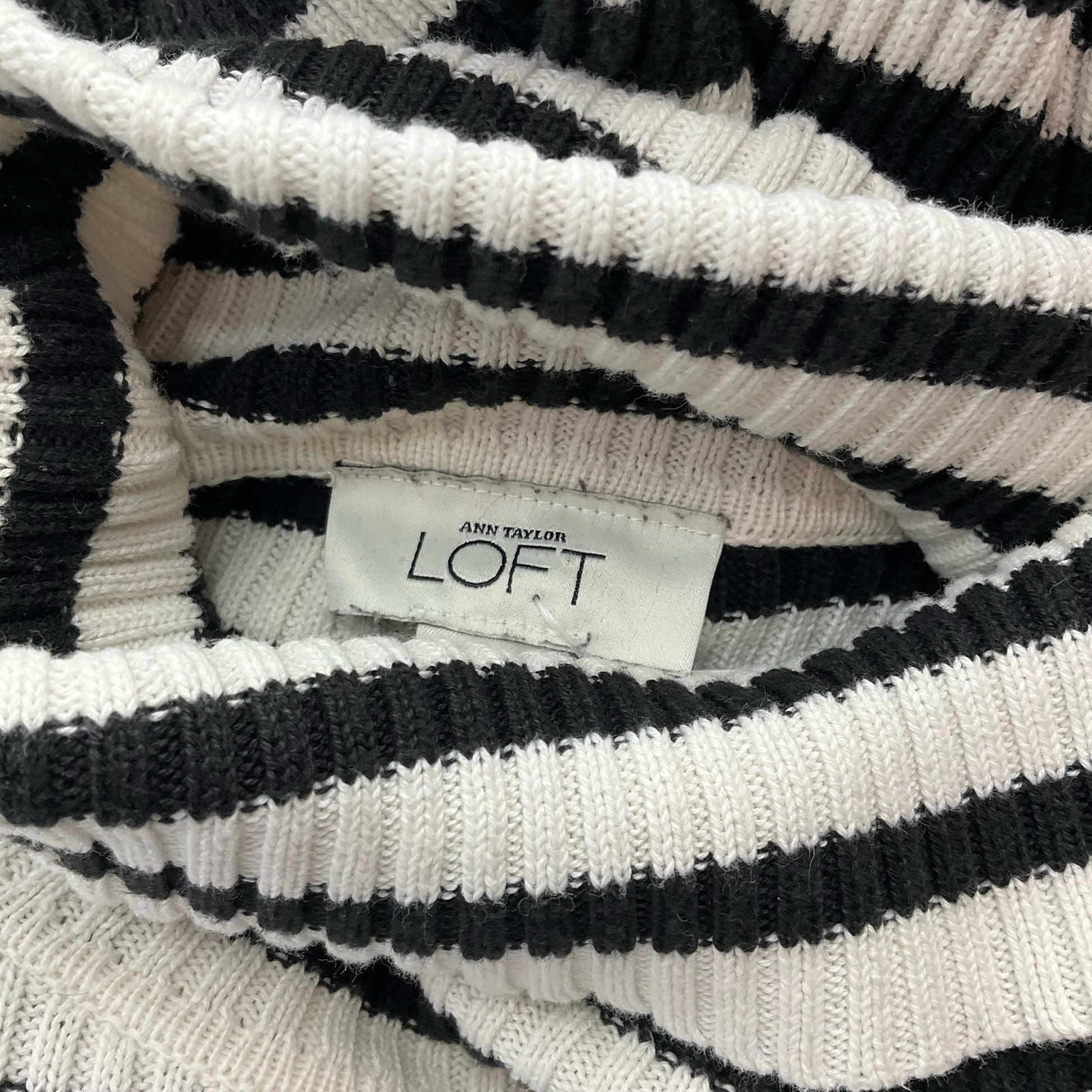 Close-up of Ann Taylor Loft label on black and white striped ribbed sweater, confirming brand authenticity for Size XS top.