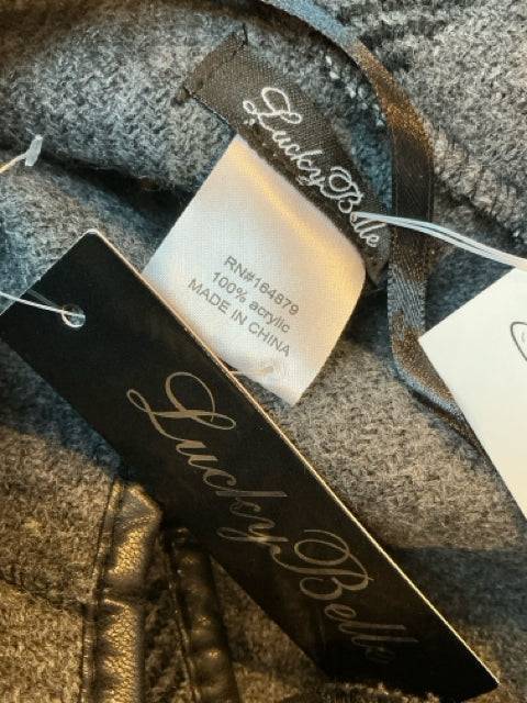 Close-up of Lucky Belle brand tags on black and gray plaid poncho, 100% acrylic, new with tags at Margaret’s Fine Consignments.