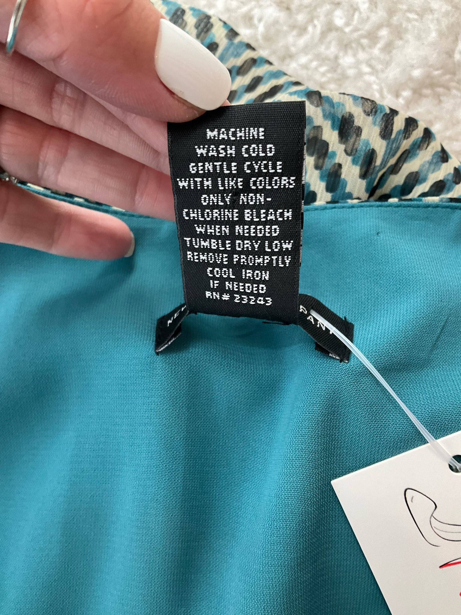 Care label of New York & Co teal/cream dress with washing instructions, emphasizing machine wash cold and tumble dry low settings.