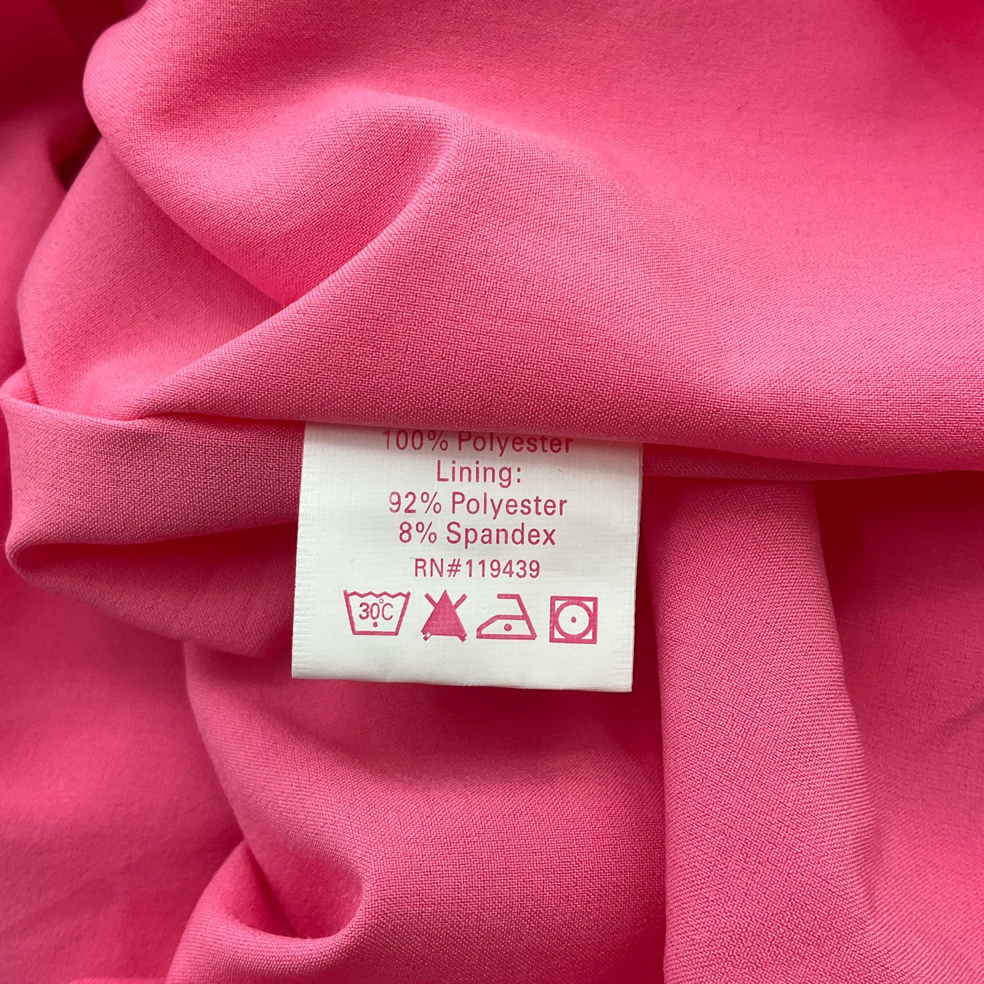 Fabric content label of Julie Brown pink dress, size 6. Made of 100% polyester with spandex-lined interior for comfort.